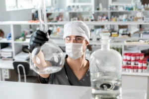 Investigador con guantes y anteojos de protección sostiene un matraz de vidrio en un laboratorio (imagen ilustrativa genérica, banco de imágenes Pexels)