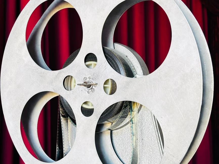 Carrete de película de cine antiguo frente a un telón rojo de teatro (imagen ilustrativa genérica, sin relación directa con el hecho puntual). Banco: Pexels, foto de Mariia Stepanova.