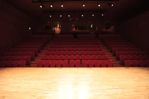 Auditorio vacío con butacas rojas y escenario iluminado (imagen ilustrativa genérica, banco de imágenes Pexels)