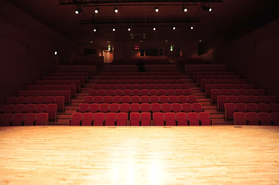 Auditorio vacío con butacas rojas y escenario iluminado (imagen ilustrativa genérica, banco de imágenes Pexels)