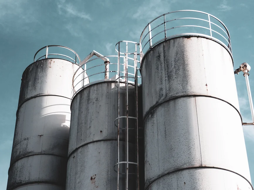 Silos industriales de almacenamiento de granos vistos desde abajo, contra un cielo despejado (banco de imágenes Pexels; imagen ilustrativa genérica)