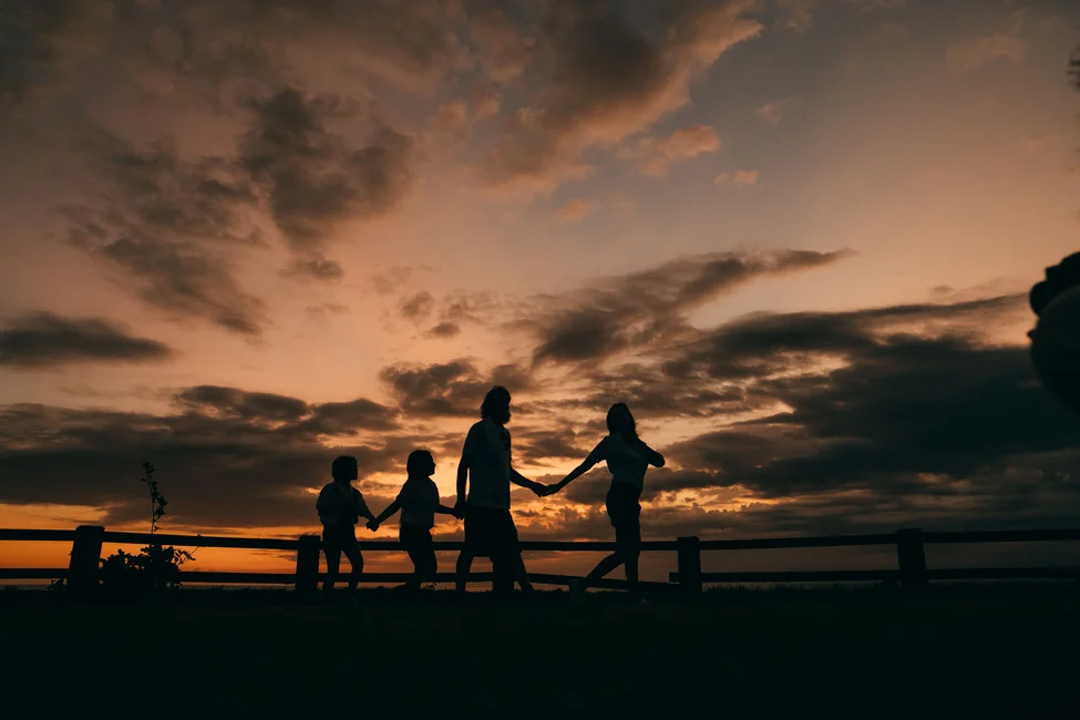Siluetas de una familia tomada de las manos al atardecer (imagen ilustrativa genérica, sin relación directa con la familia protagonista de la nota). Banco: Pexels, foto de Mikhail Nilov.