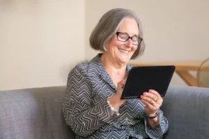 Mujer adulta mayor sonriendo mientras usa una tablet (imagen ilustrativa genérica, banco de imágenes Pexels)