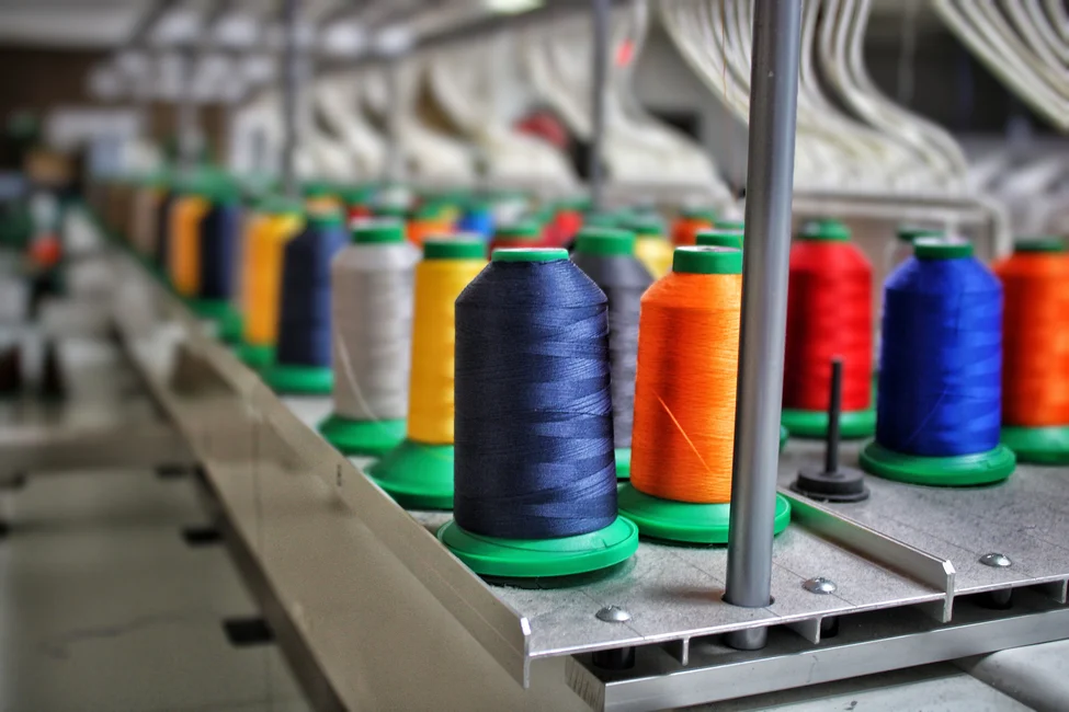 Conos de hilado de colores en una máquina textil (imagen ilustrativa genérica)