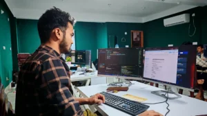 Persona trabajando con computadoras en una oficina (imagen ilustrativa genérica). Banco de imágenes: Pexels, foto de Zayed Hossain.